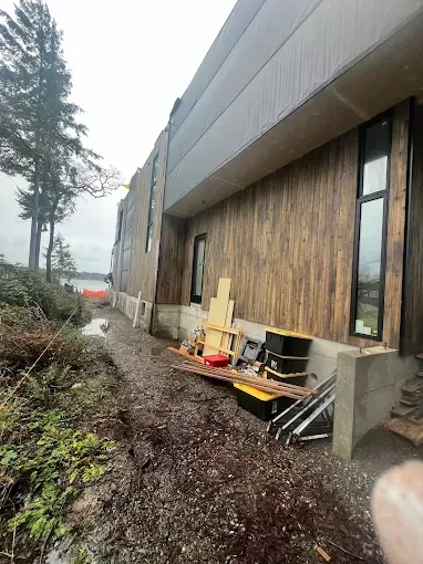 Construction site: exterior of a modern building with wood siding and a concrete foundation, tools scattered on the ground.