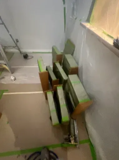 Cabinets taped and stacked in a room under renovation. Green tape, white walls, brown cardboard, and tools are visible.