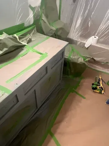 Bathroom vanity masked with green tape, covered in plastic, ready for painting.