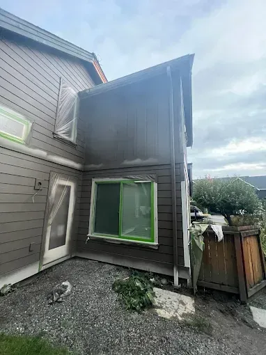 House exterior being painted brown; windows and door taped for protection.