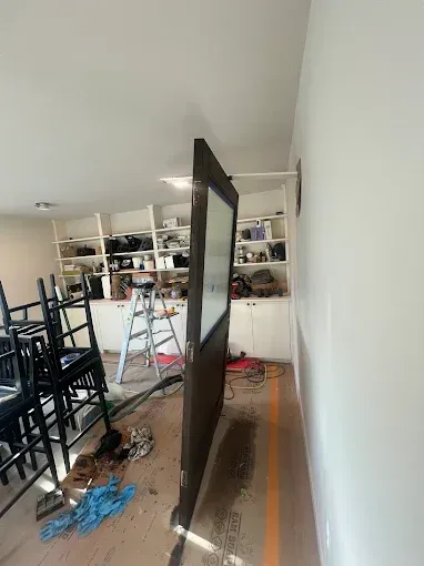 A dark-colored door is being installed; construction tools and materials are scattered around the room.