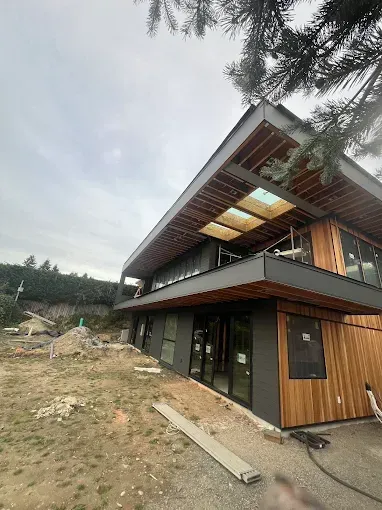 Modern house under construction with wood and dark siding, large windows, and skylights.
