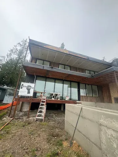 Modern house under construction with large windows, wood accents, and a ladder.