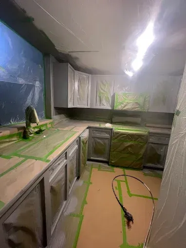 Kitchen cabinets and counters being painted gray, protected by green tape and plastic.