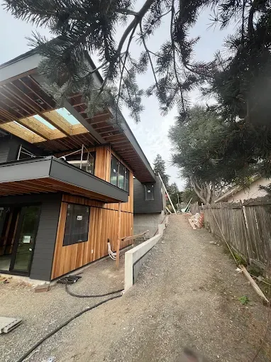 Modern two-story house with wood siding and gray accents under construction next to a gravel driveway.