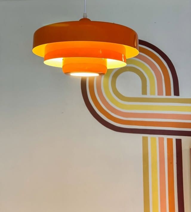 Orange tiered pendant lamp hangs against a wall with a retro rainbow design.