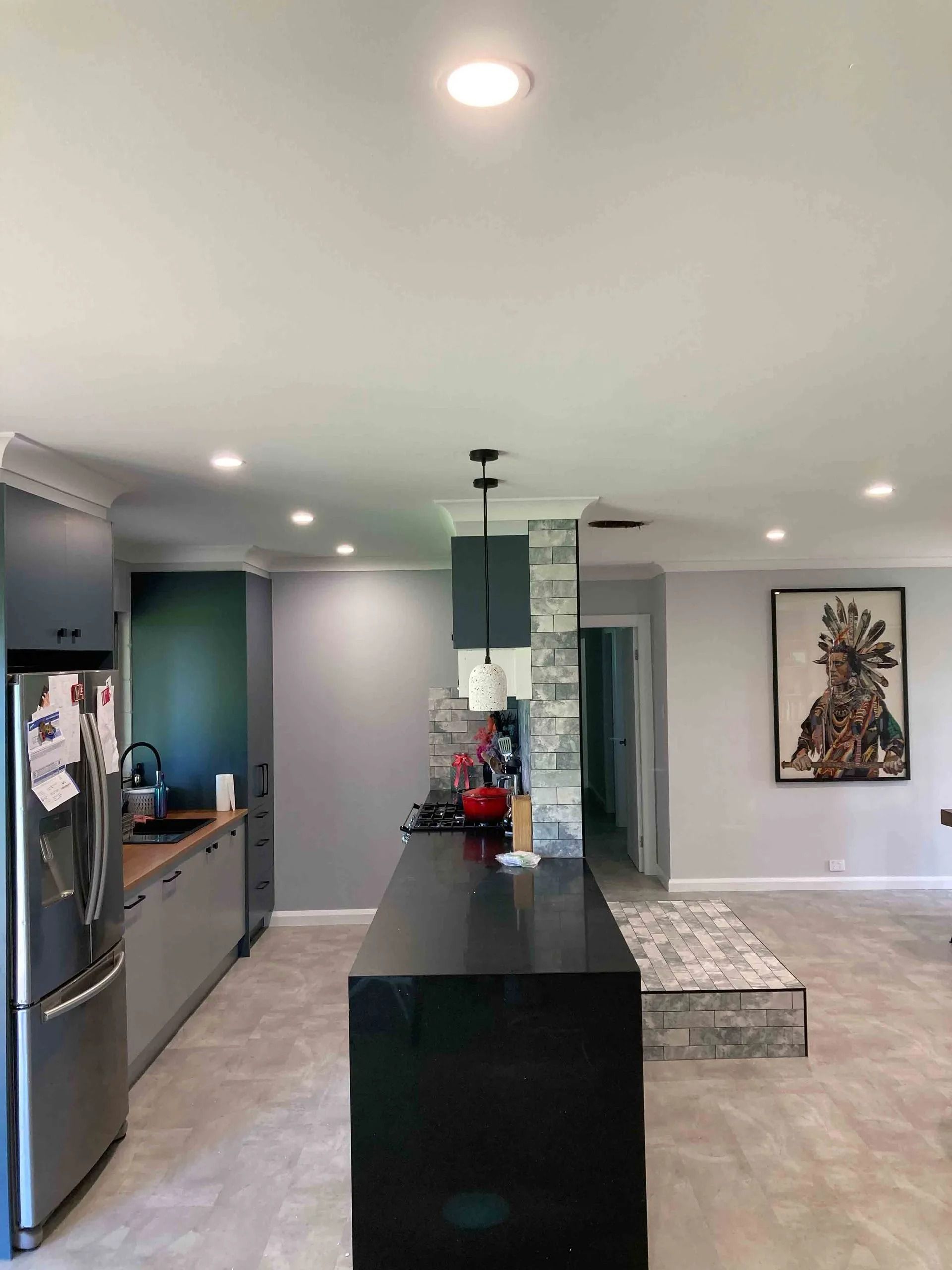 Modern kitchen with black island, gray cabinets, artwork, and recessed lighting.