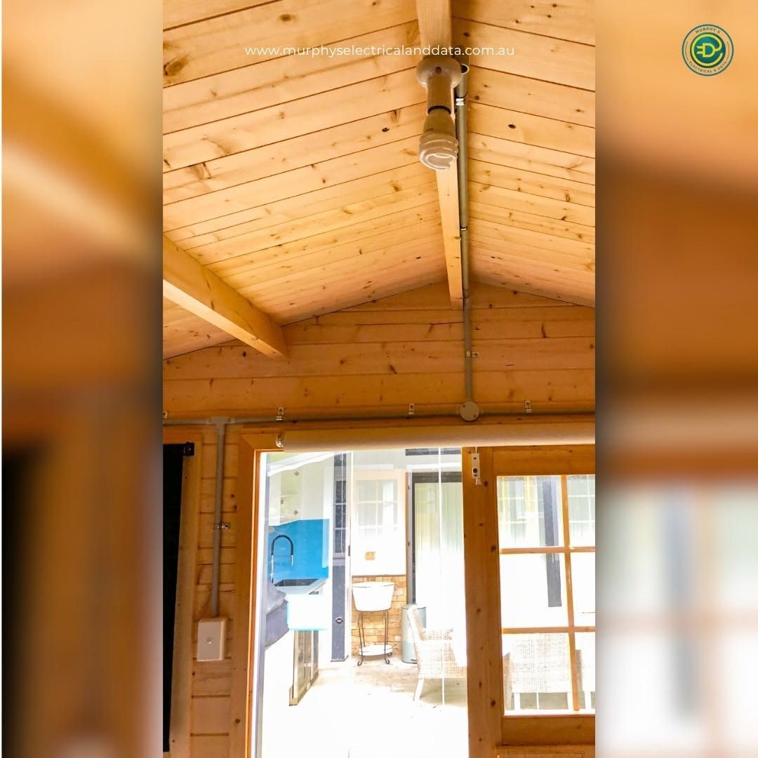 Interior view of a wooden structure with electrical conduit and lighting fixtures; open doorway.