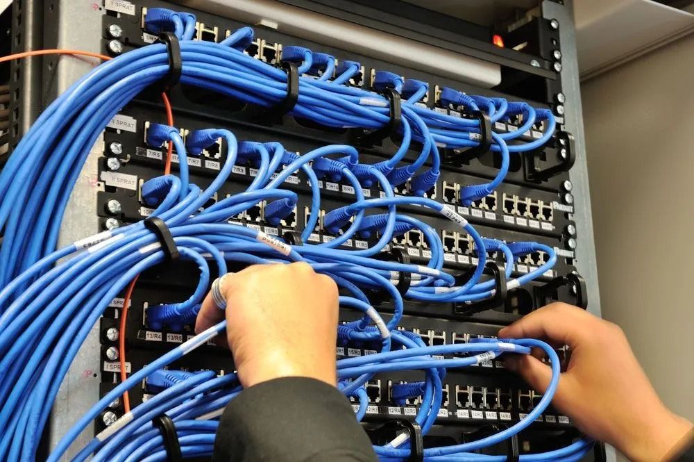 Hands connecting blue network cables to server rack.