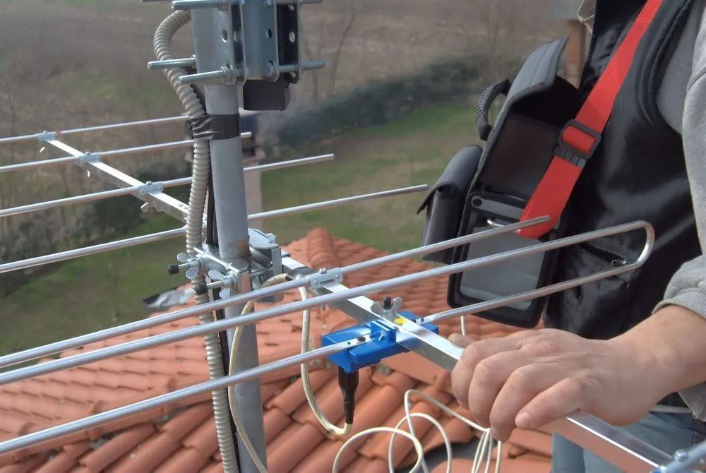 Person on roof adjusting a TV antenna. Antenna is metal, roof is tiled.