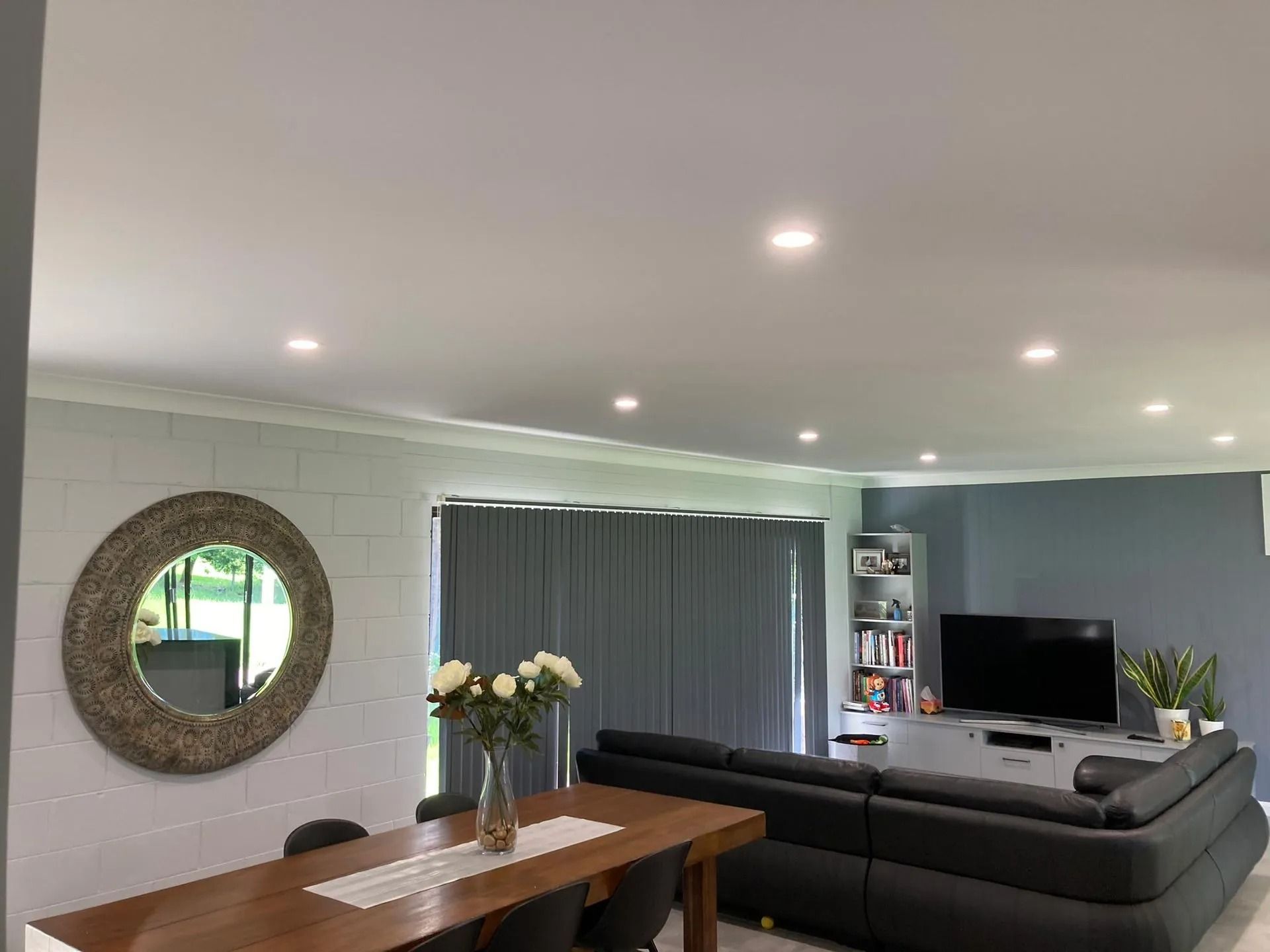 Living room with dining table, sectional sofa, TV, and round mirror. Gray curtains and walls.