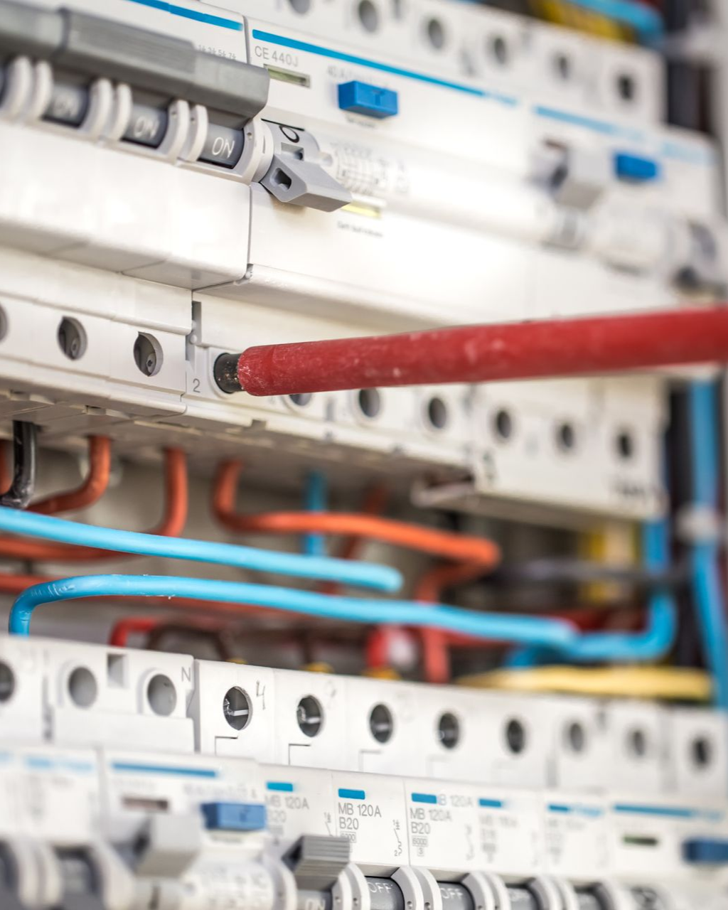 A screwdriver tip touches a screw terminal inside an electrical distribution board filled with circuit breakers.