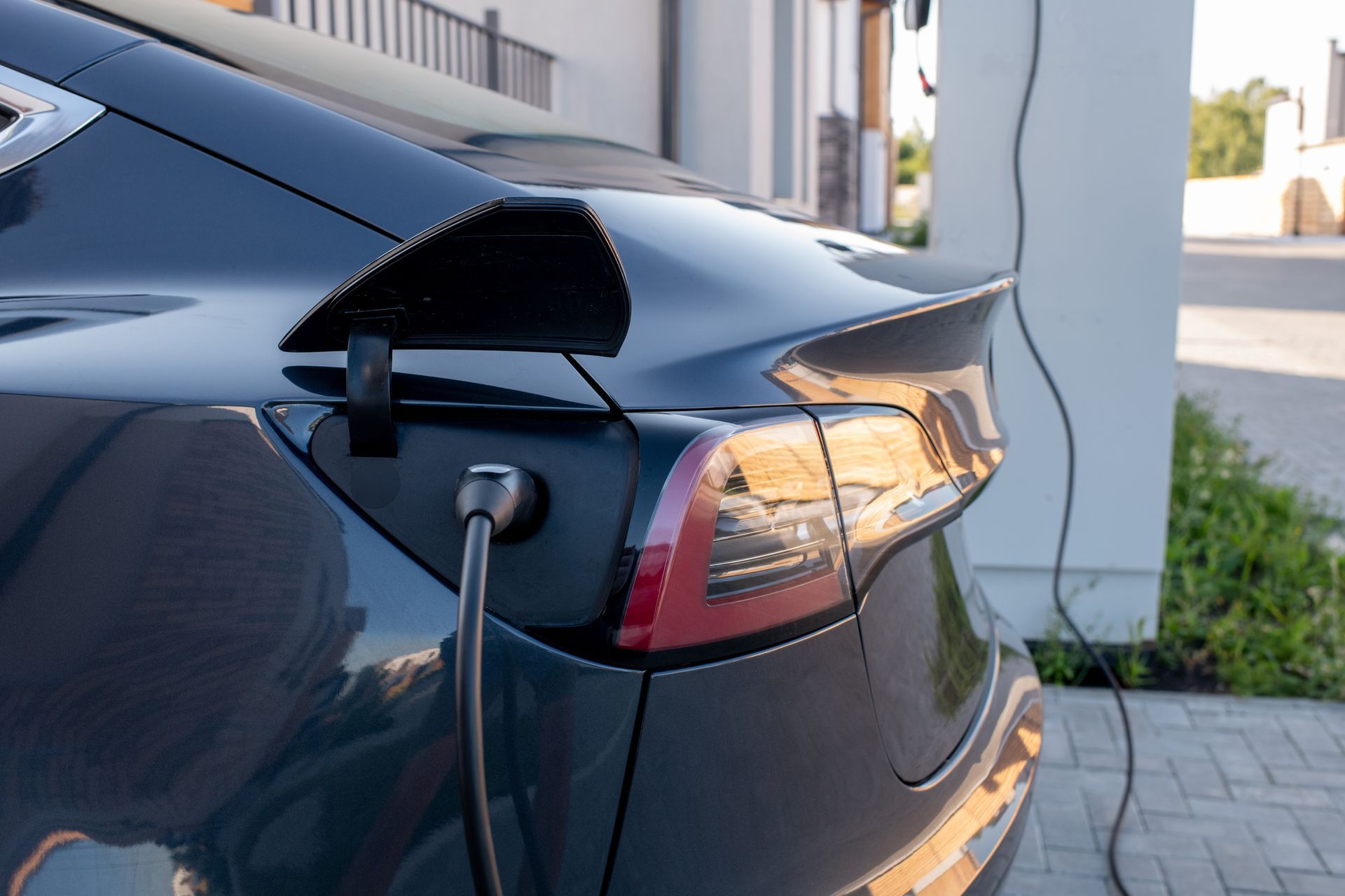 A dark blue electric car parked in a modern carport, connected to a wall-mounted white EV charging station by a cable.