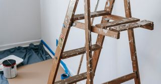 A wooden ladder is sitting in a room next to a paint can.