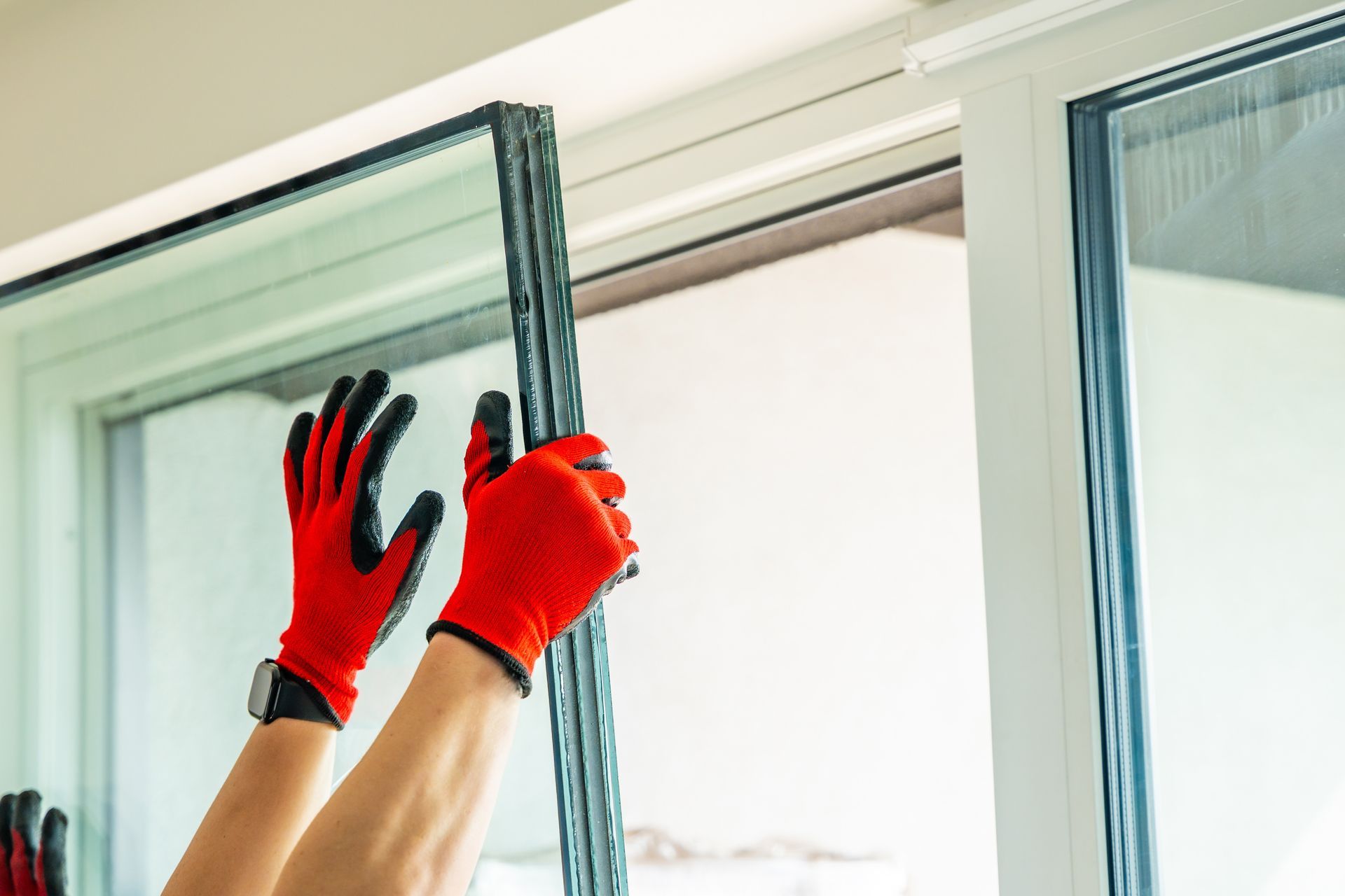 Hands wearing red gloves installing a glass window pane into a white frame.