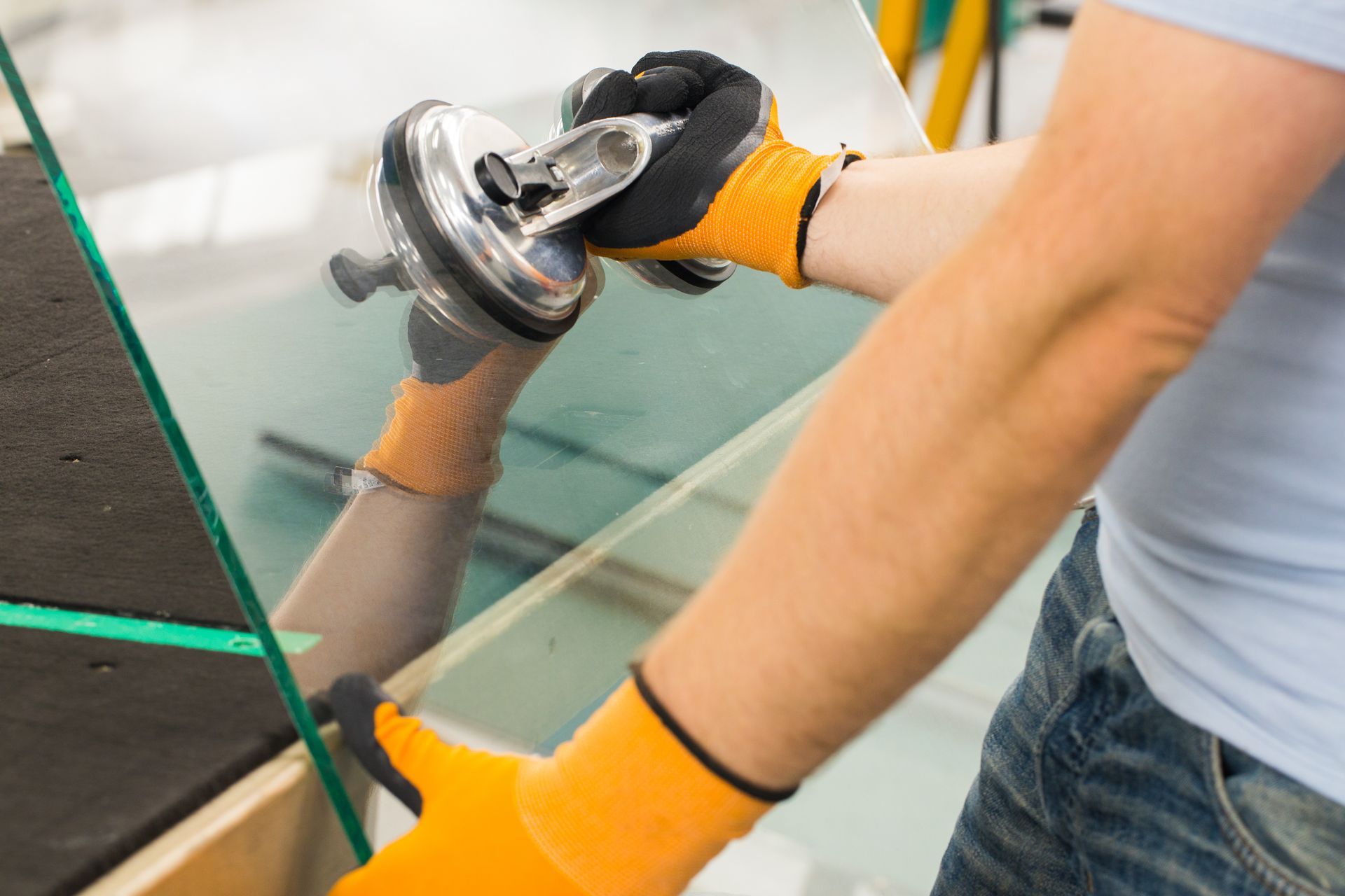 Gloved hands lifting a glass panel with a suction cup tool.