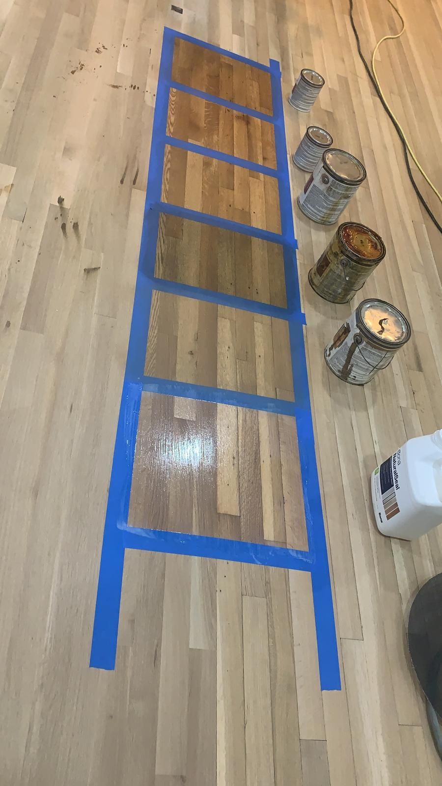 A ladder is taped to a wooden floor next to paint cans.