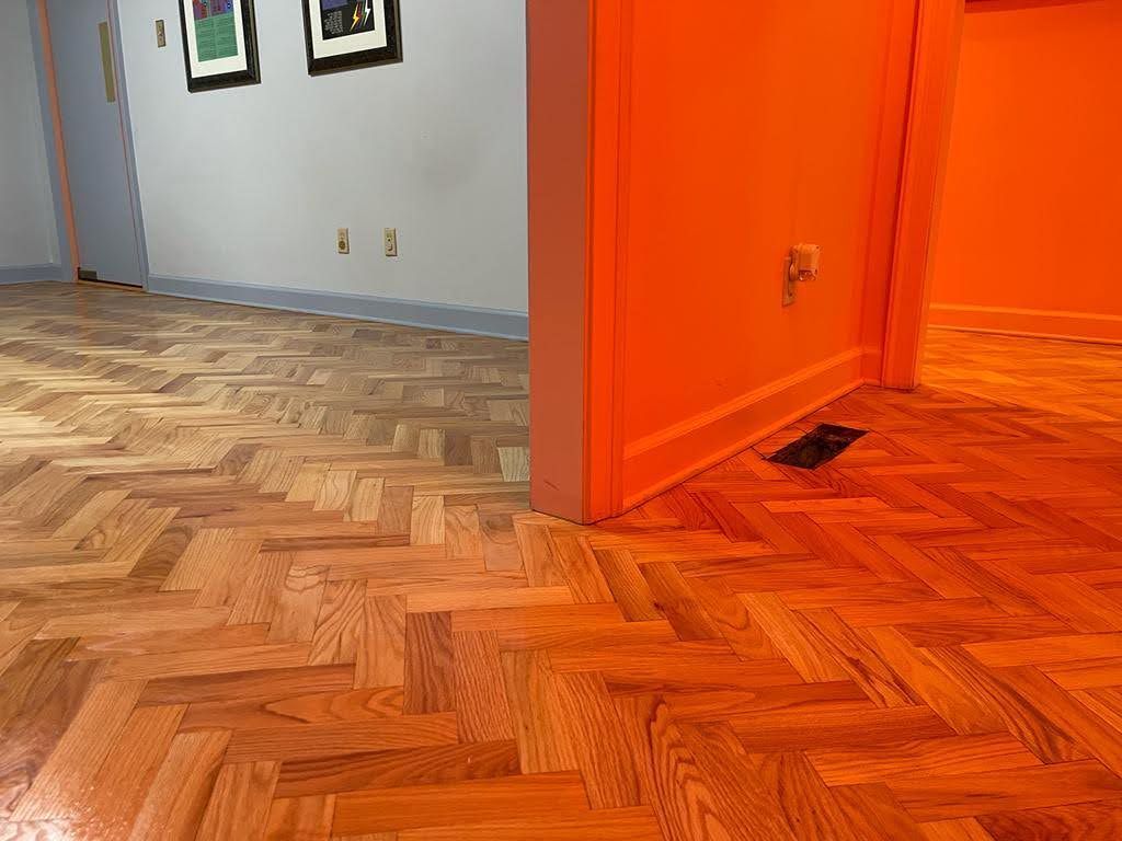A wooden floor with a herringbone pattern in a room with orange walls.