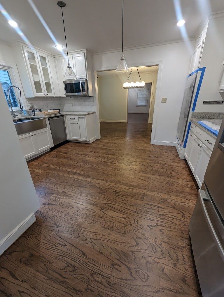 A kitchen with hardwood floors , white cabinets and stainless steel appliances.