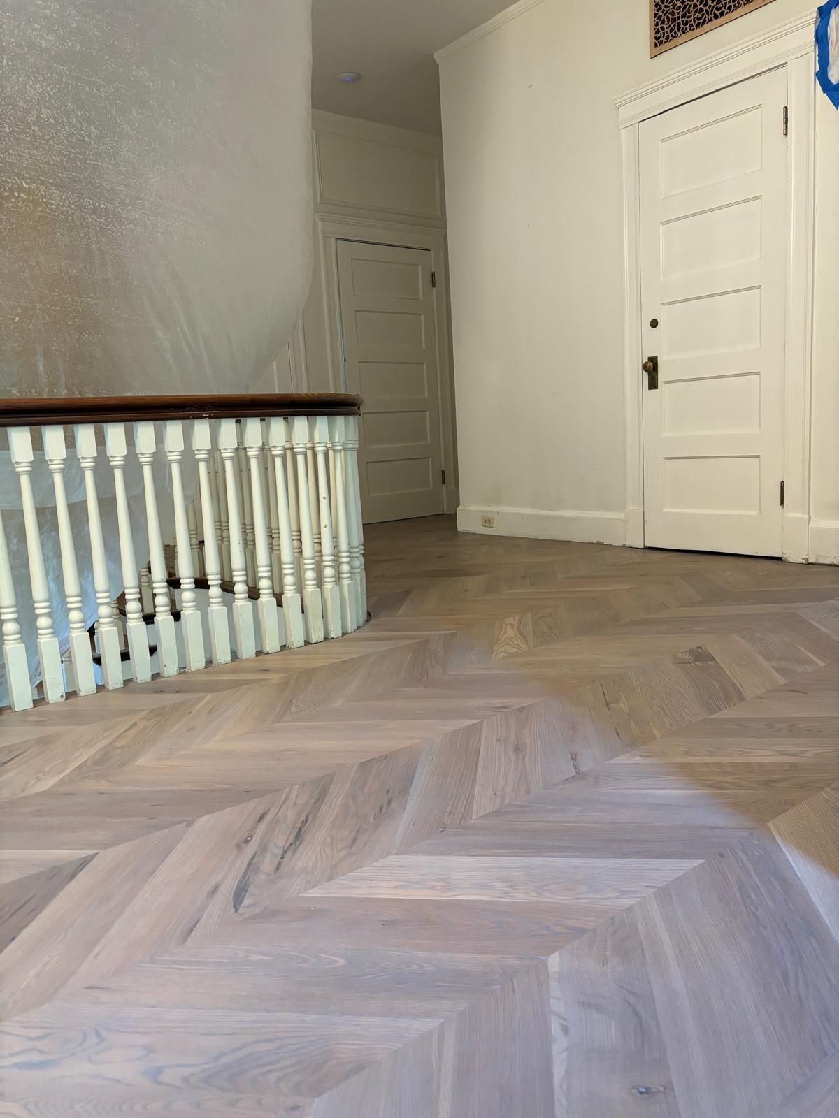 A wooden floor with a herringbone pattern and a white railing in a hallway.