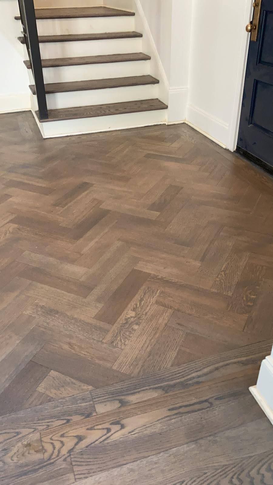 A wooden floor with a herringbone pattern and stairs in the background.