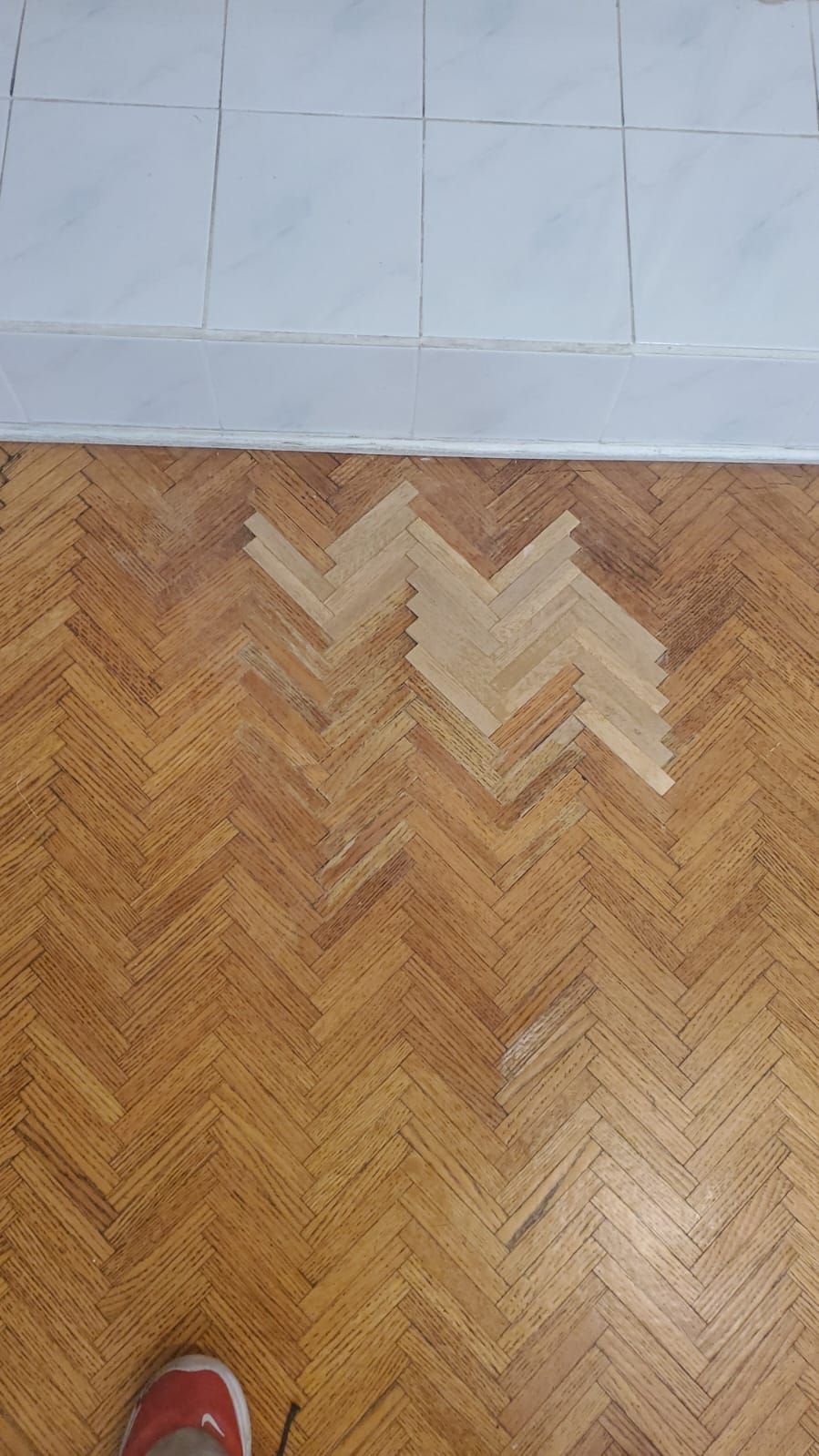 A person is standing on a wooden floor with a herringbone pattern.