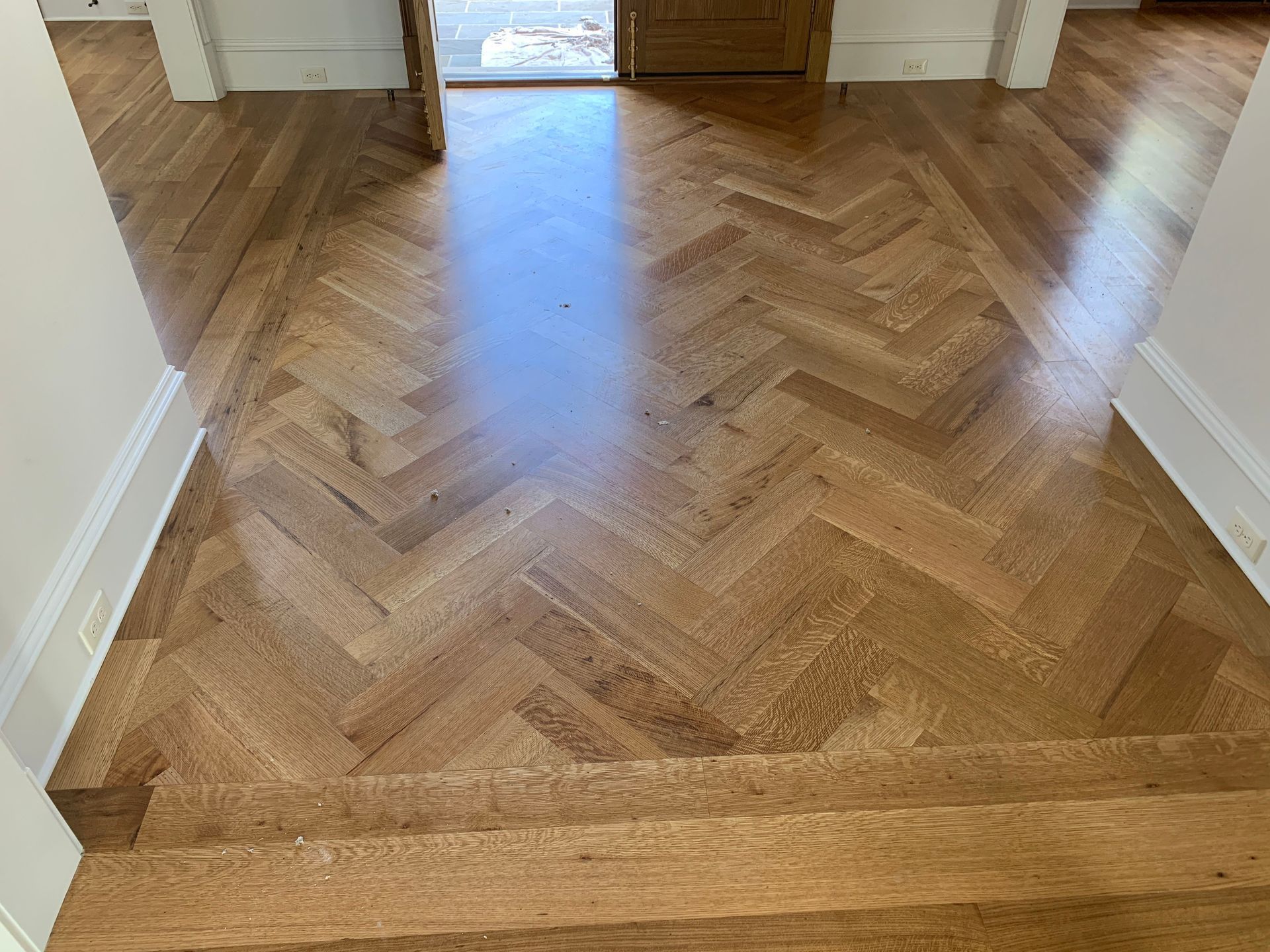 A wooden floor with a herringbone pattern in a hallway.