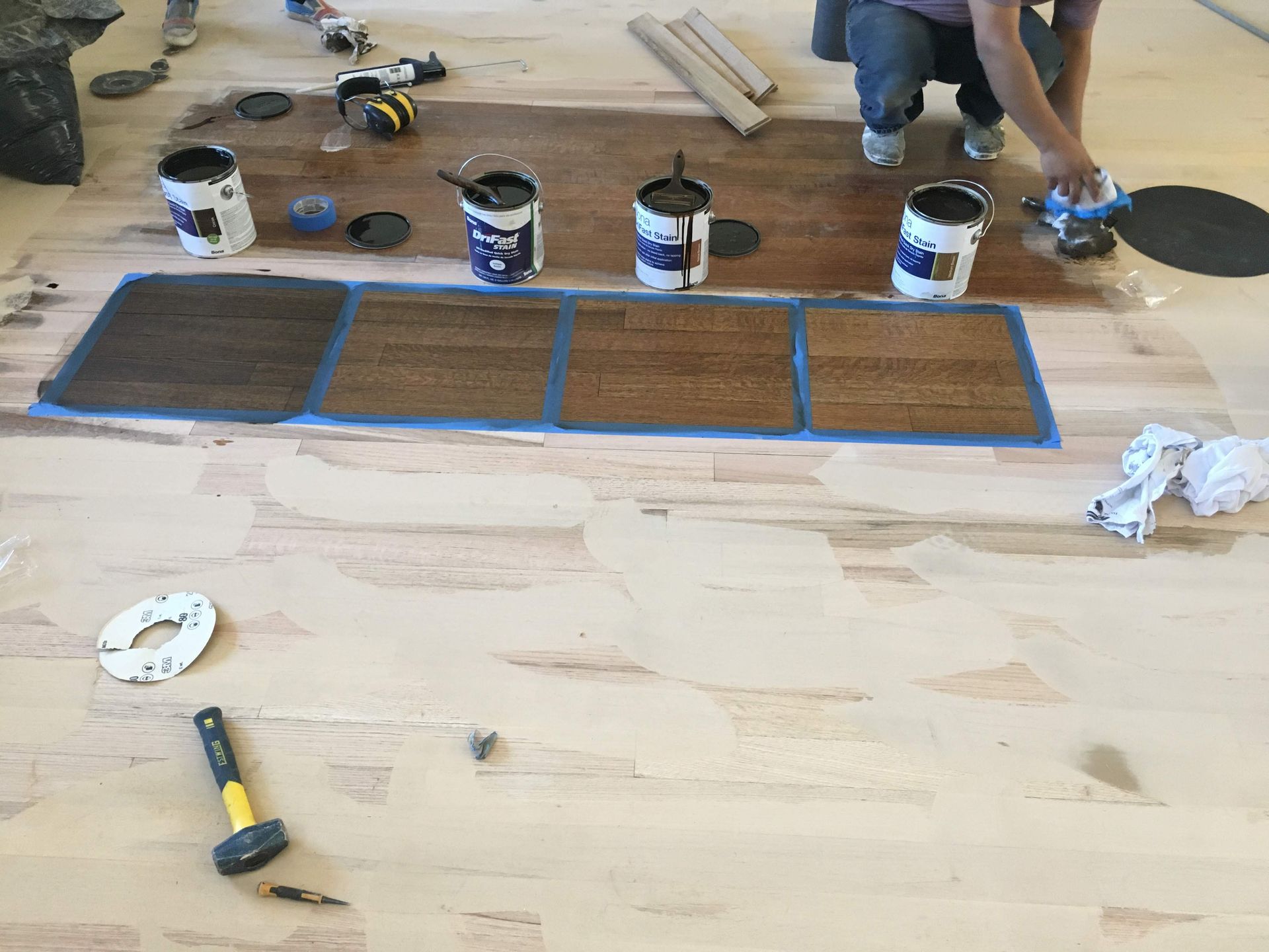 A man is painting a wooden floor with buckets of paint.