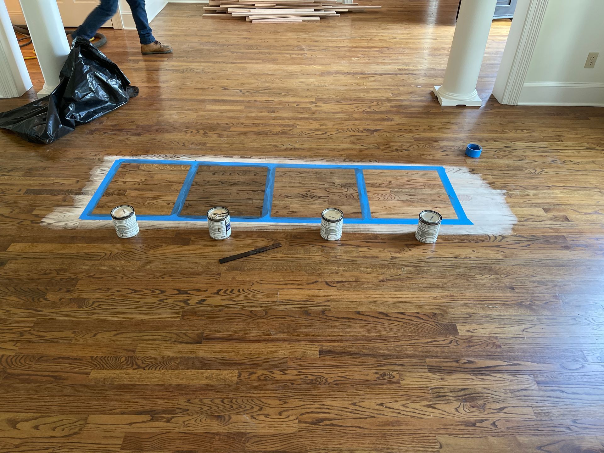 A wooden floor is being painted with a blue tape.