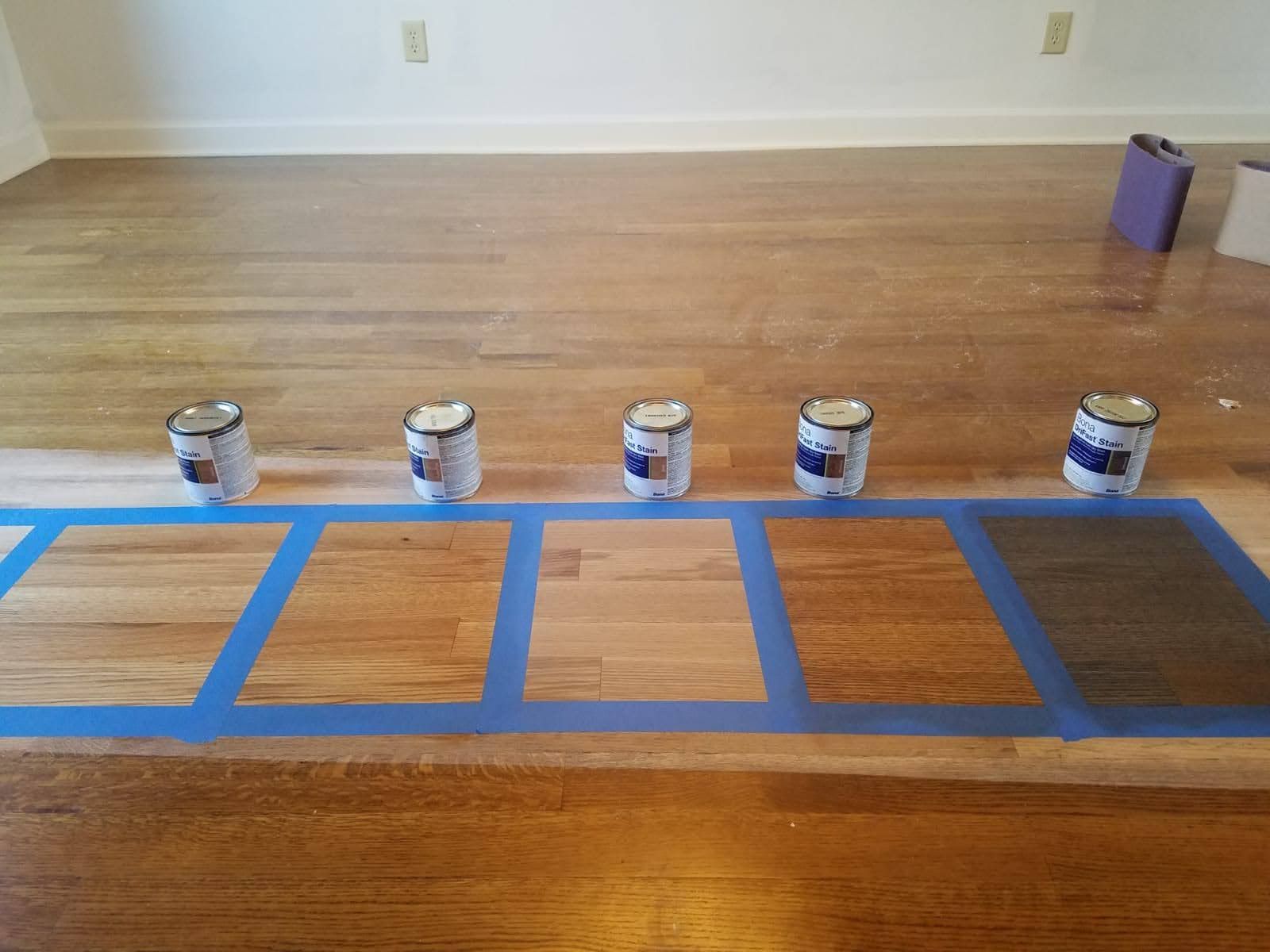 Five cans of paint are lined up on a wooden floor.