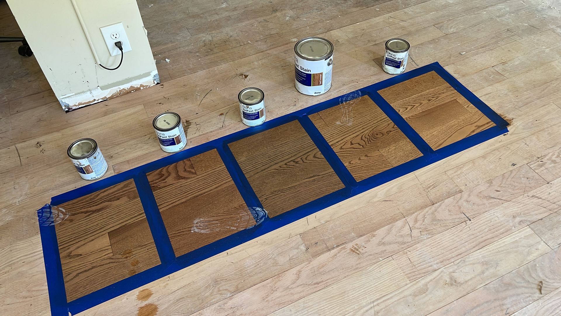 A row of cans of paint are sitting on a wooden floor.