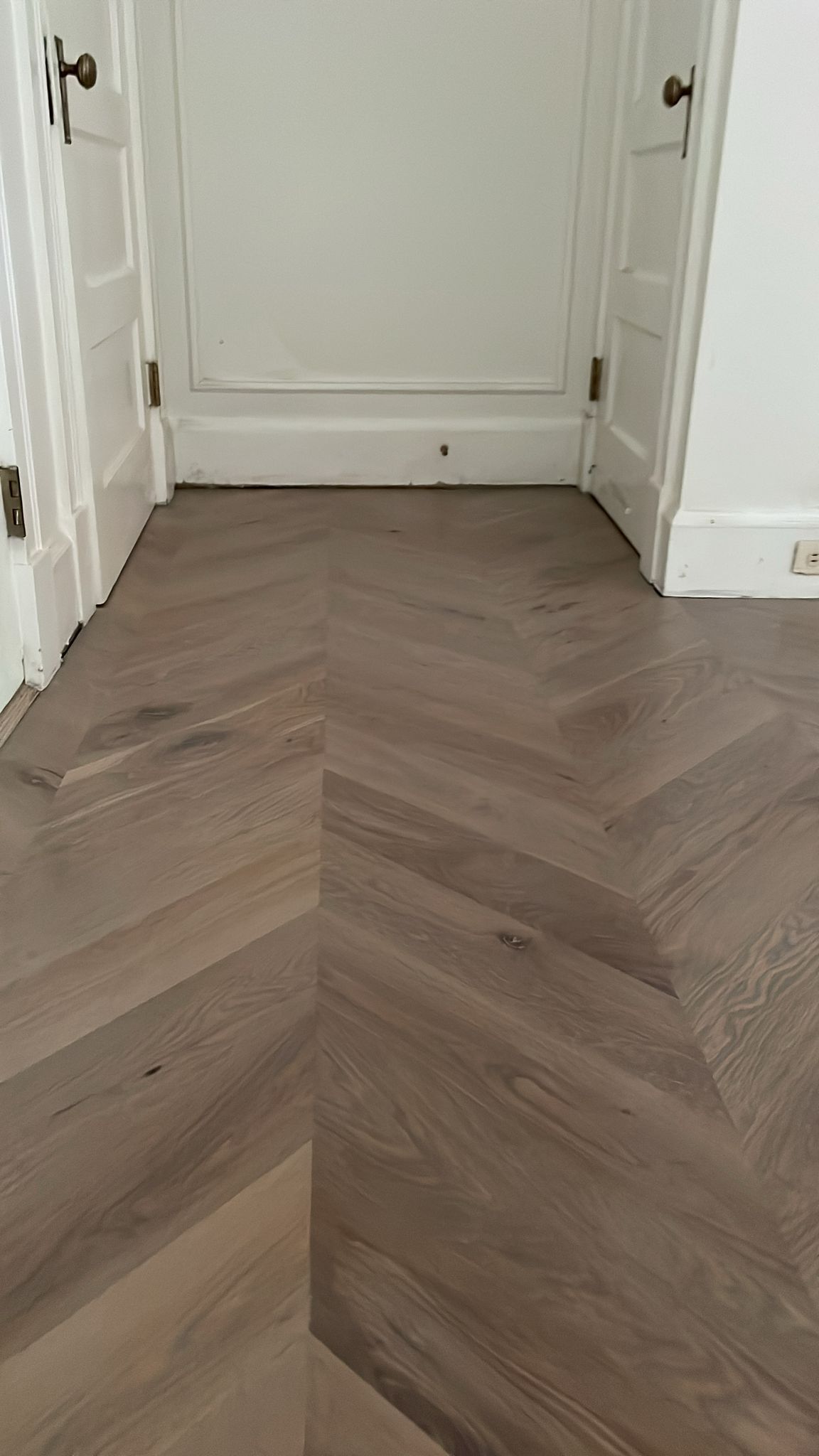 A wooden floor with a herringbone pattern in a hallway.