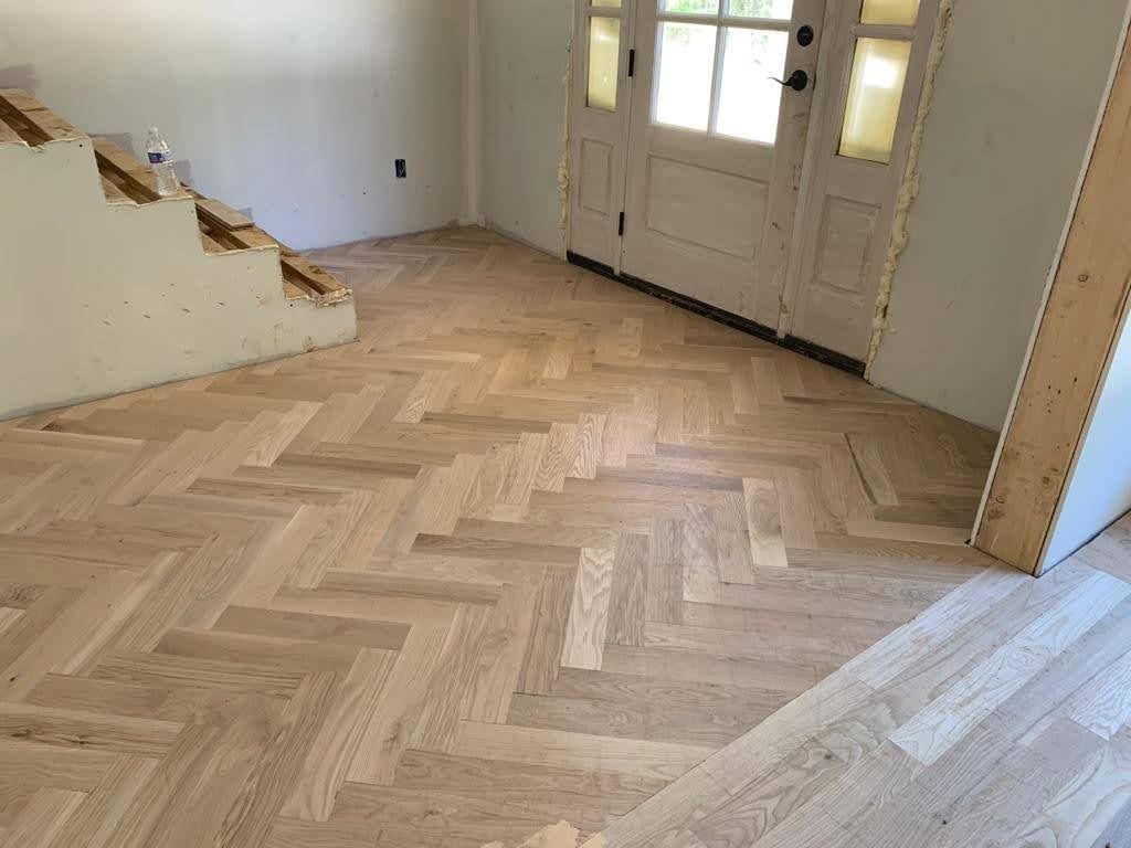 A room with a herringbone wooden floor and stairs.