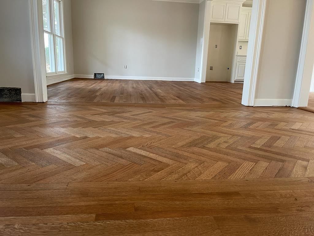 A large empty room with a wooden floor and a herringbone pattern.