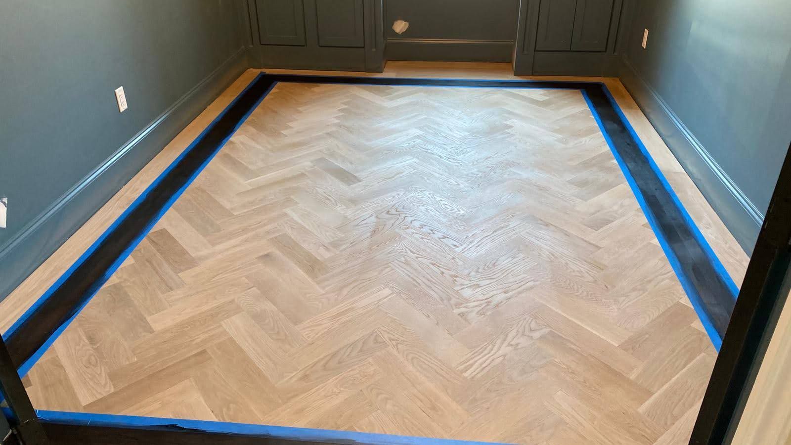 A wooden floor with a herringbone pattern is being painted in a room.