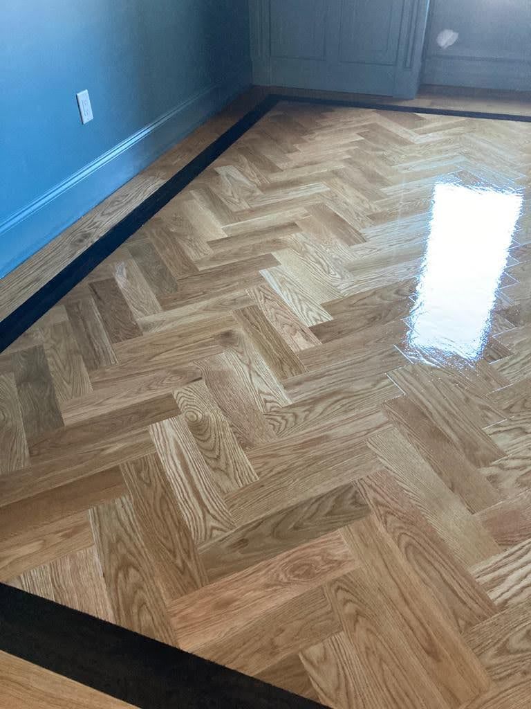 A wooden floor with a herringbone pattern and a black border in a room.
