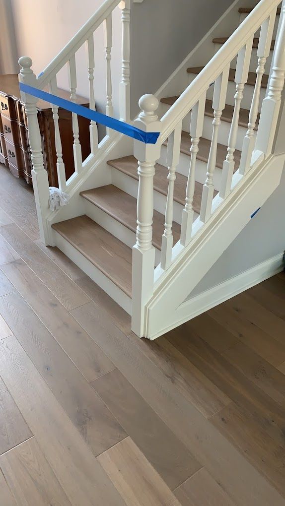 A white staircase with wooden steps and a blue tape on the railing.