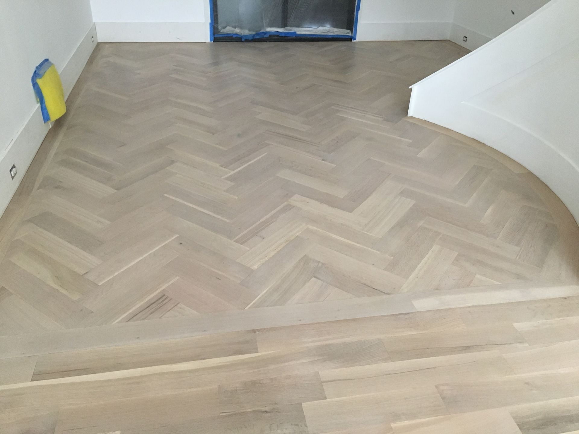 A wooden floor with a herringbone pattern and stairs