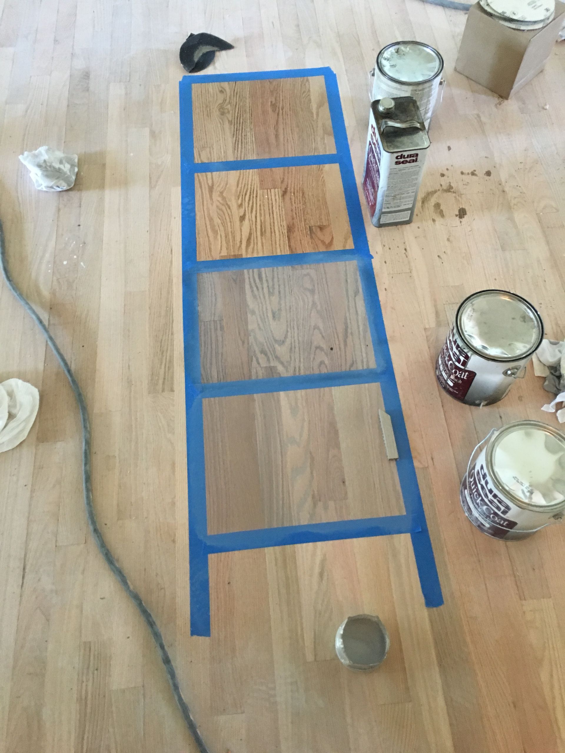 A ladder is taped to a wooden floor next to paint cans.