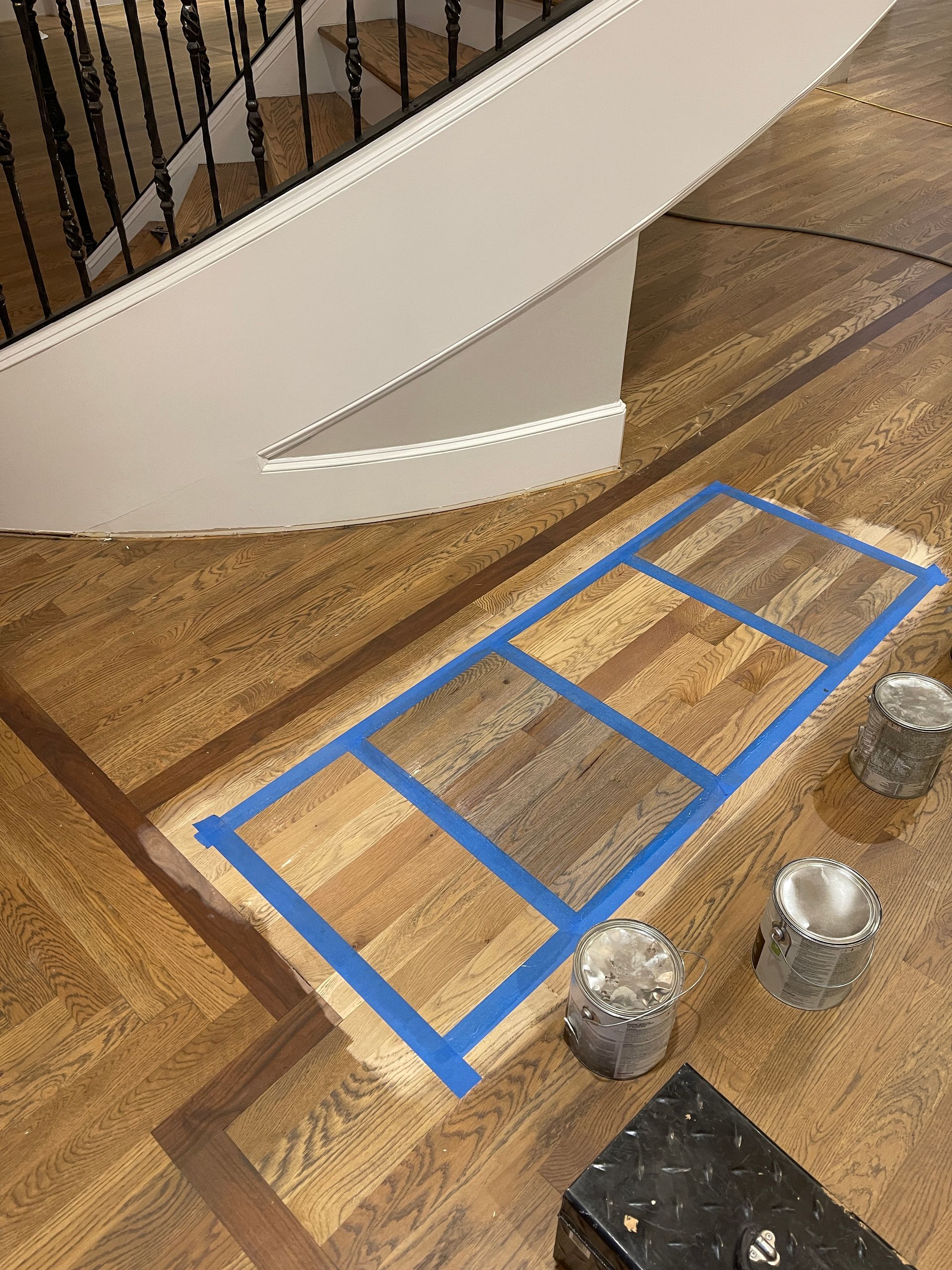 A wooden floor with blue tape on it and a staircase in the background.