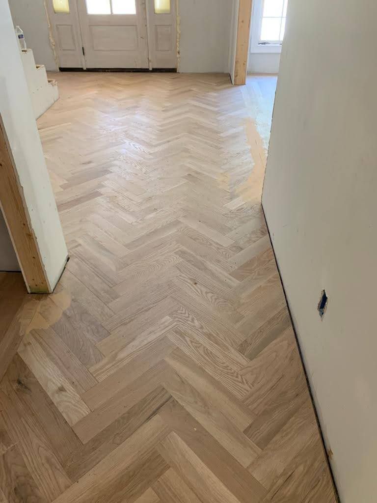 A wooden floor with a herringbone pattern in a hallway.