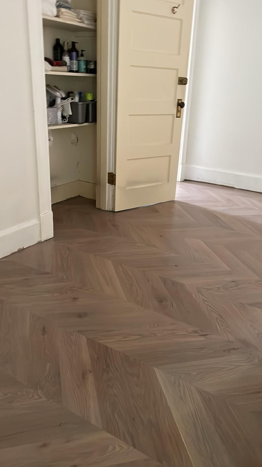 A room with a wooden floor , a door , and a shelf.