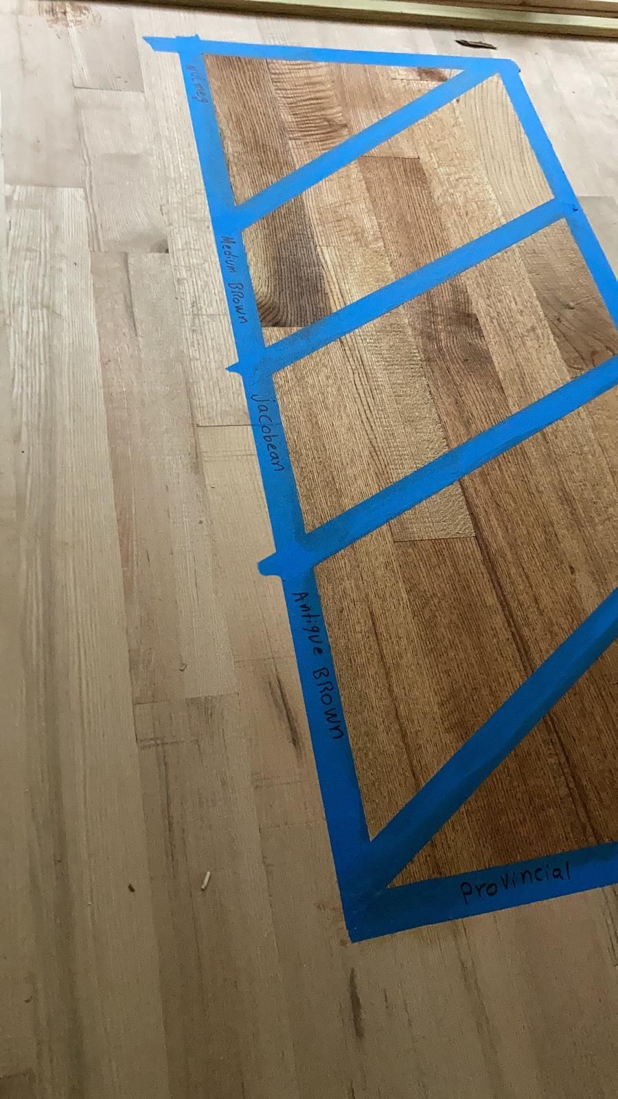 A piece of wood is taped to the floor with blue tape.