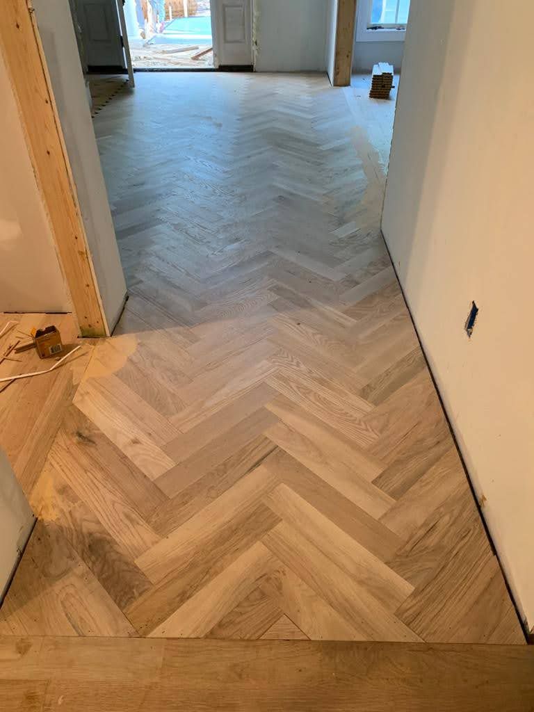 A wooden floor with a herringbone pattern is being installed in a hallway.