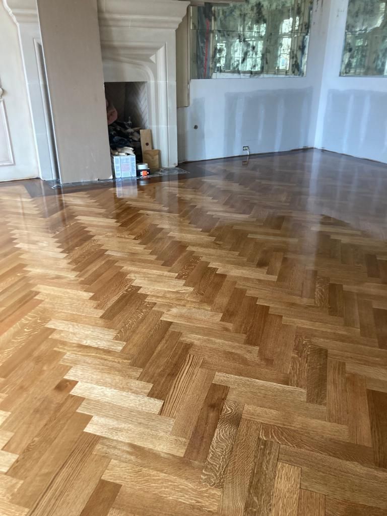A living room with a herringbone wooden floor and a fireplace.