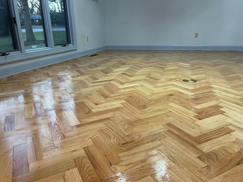 A room with a herringbone wooden floor and a window.