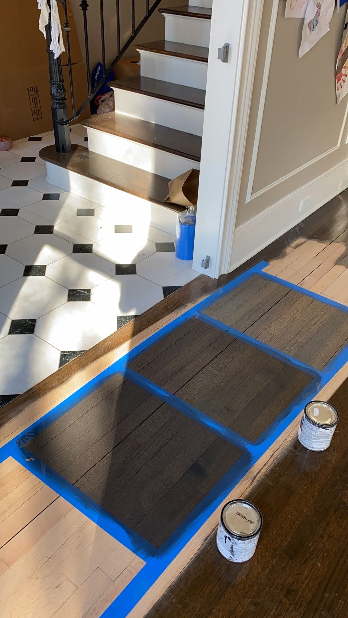 A wooden floor is being painted in a hallway next to a staircase.