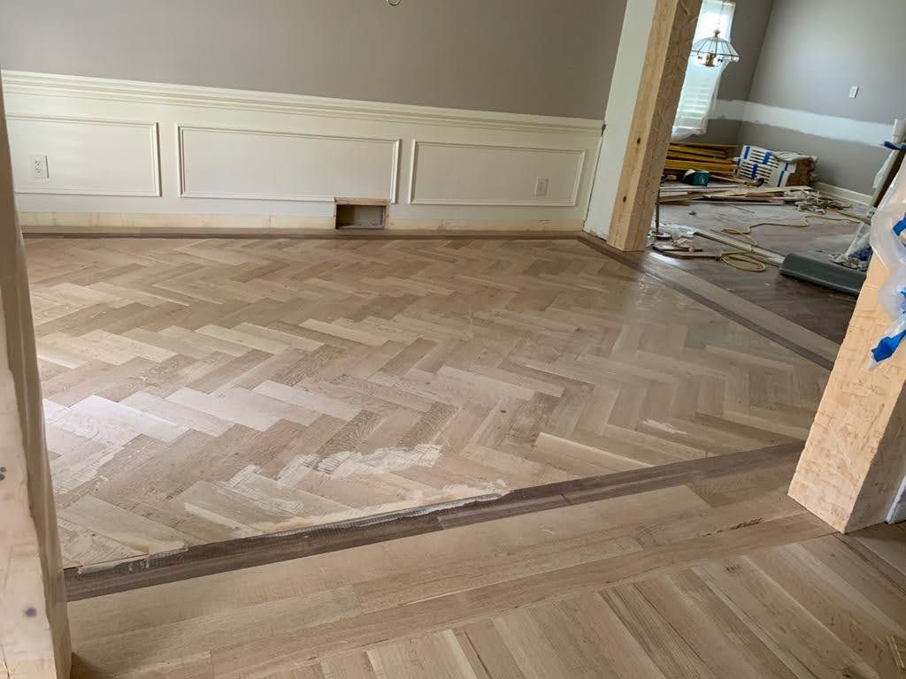 A wooden floor with a herringbone pattern is being installed in a living room.