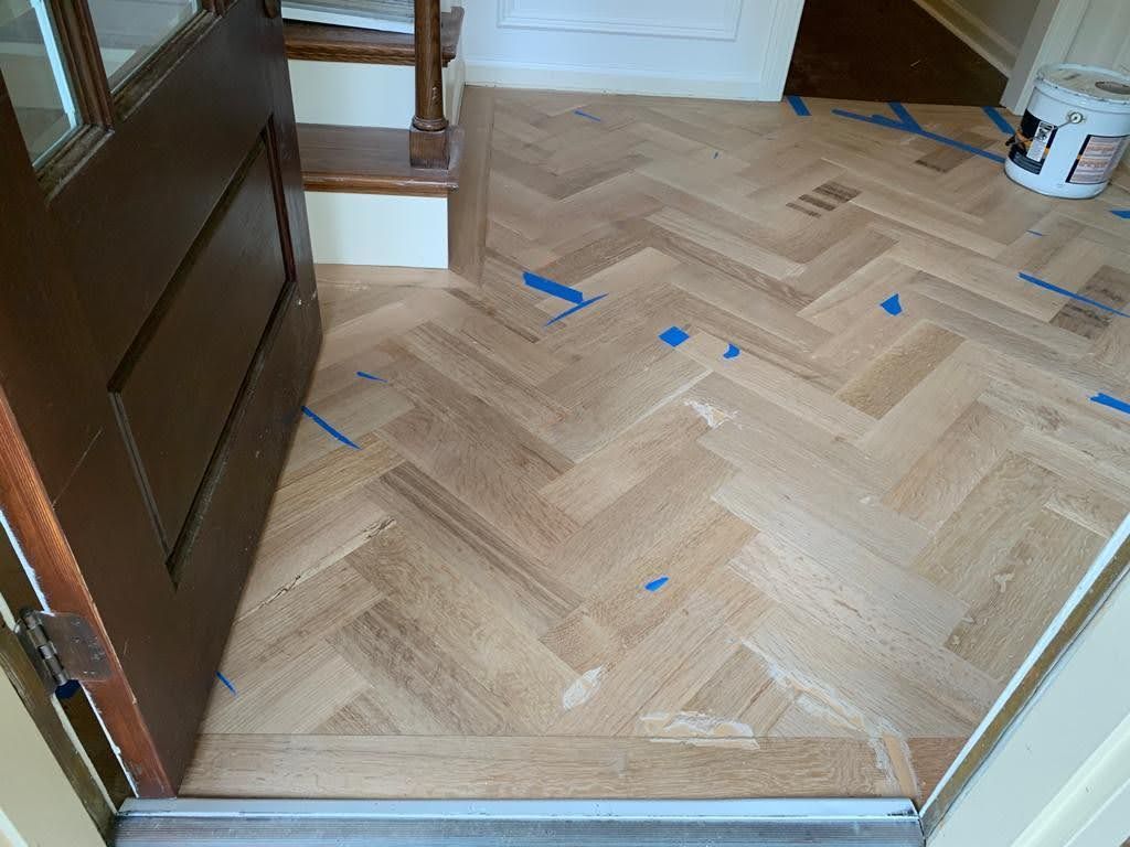 A wooden floor with a herringbone pattern is being painted in a room.