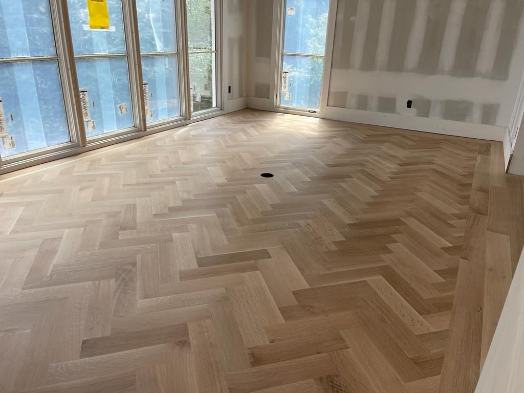 A living room with a herringbone wooden floor and lots of windows.